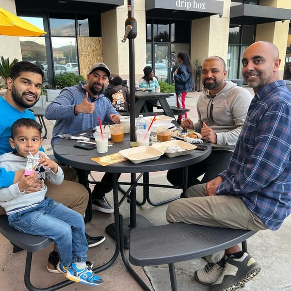 Four men and a child enjoy Indian food and drinks at an outdoor table at Great Indian Kitchen.