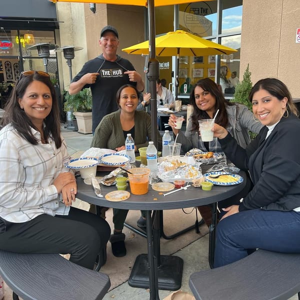 Five people, including a man in a "The Hub" shirt, enjoying Indian food at an outdoor table.