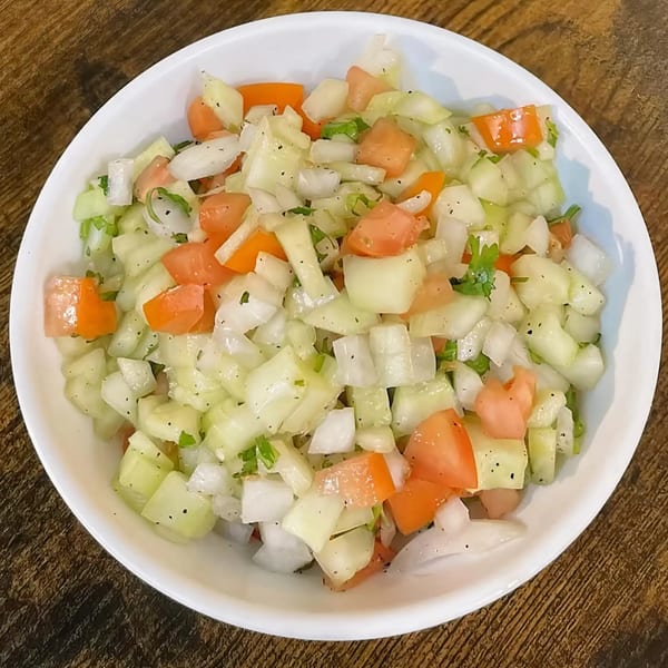 A white bowl filled with a fresh Indian salad of diced cucumbers, tomatoes, and onions.