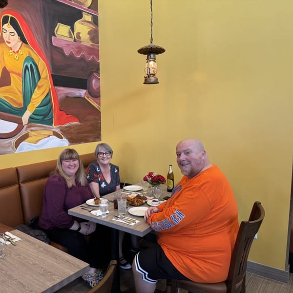 Three happy diners seated at a table in Great Indian Kitchen, with a vibrant Indian mural behind them.