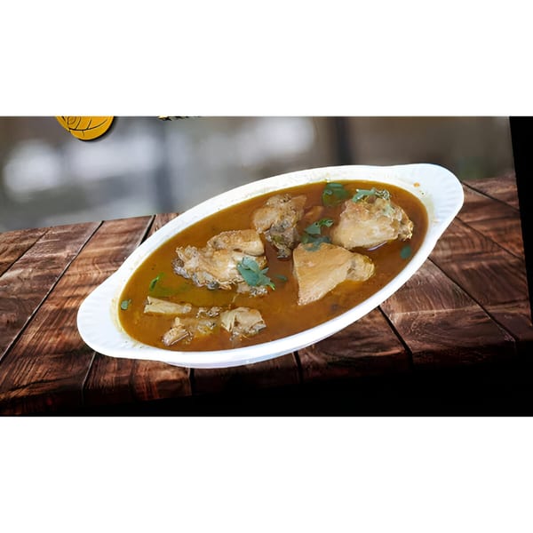 Indian chicken curry with cilantro in a white oval dish on a rustic wooden table.