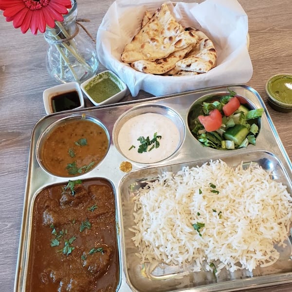 An Indian thali with rice, curry, dal, raita, salad, and naan bread, with chutneys and a red flower.