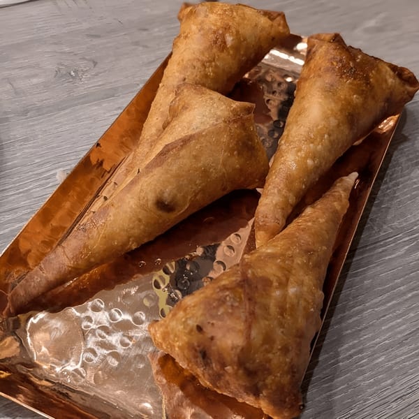 Golden-brown, crispy Indian samosas, cone-shaped, arranged on a decorative copper tray.